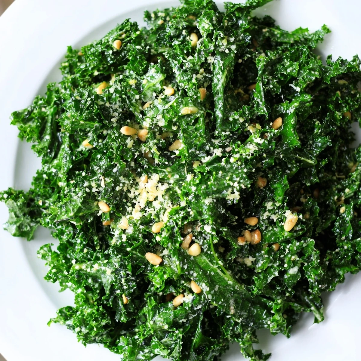 Bright garlic lemon Parmesan kale salad tossed with golden pine nuts on a rustic plate