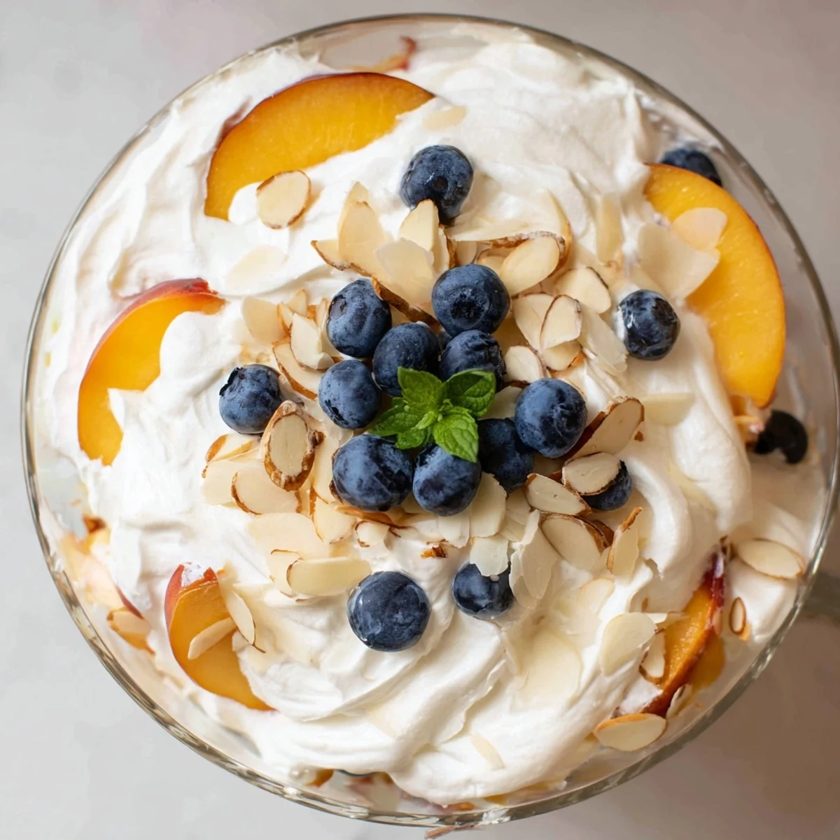 Creamy peaches and cream salad topped with fresh mint leaves in a glass bowl
