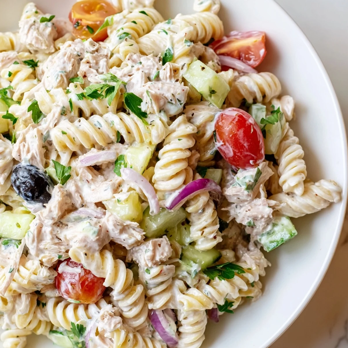 Creamy tuna pasta salad in a bowl with cherry tomatoes, celery, and fresh herbs