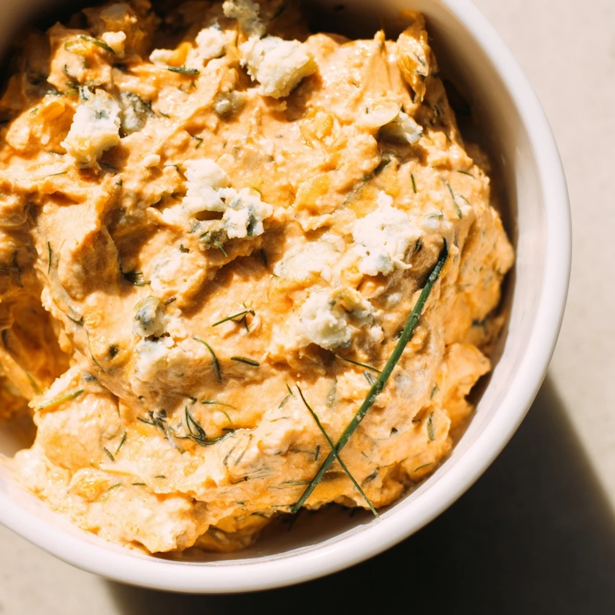Tangy buffalo pickle dip topped with cheddar cheese and fresh chives in a white ceramic dish