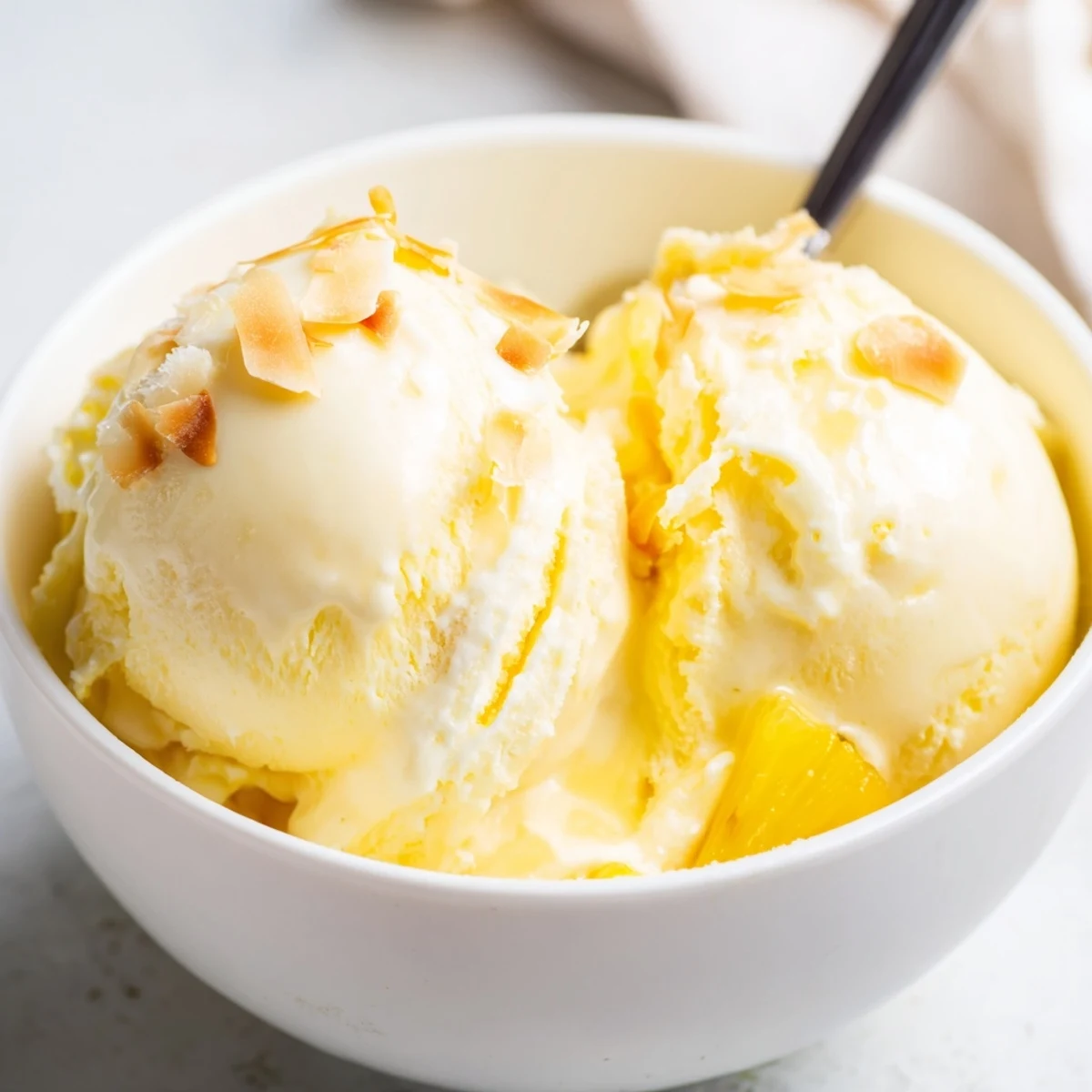 Homemade Creamy Pineapple Ice Cream churned smooth, garnished with toasted coconut.  