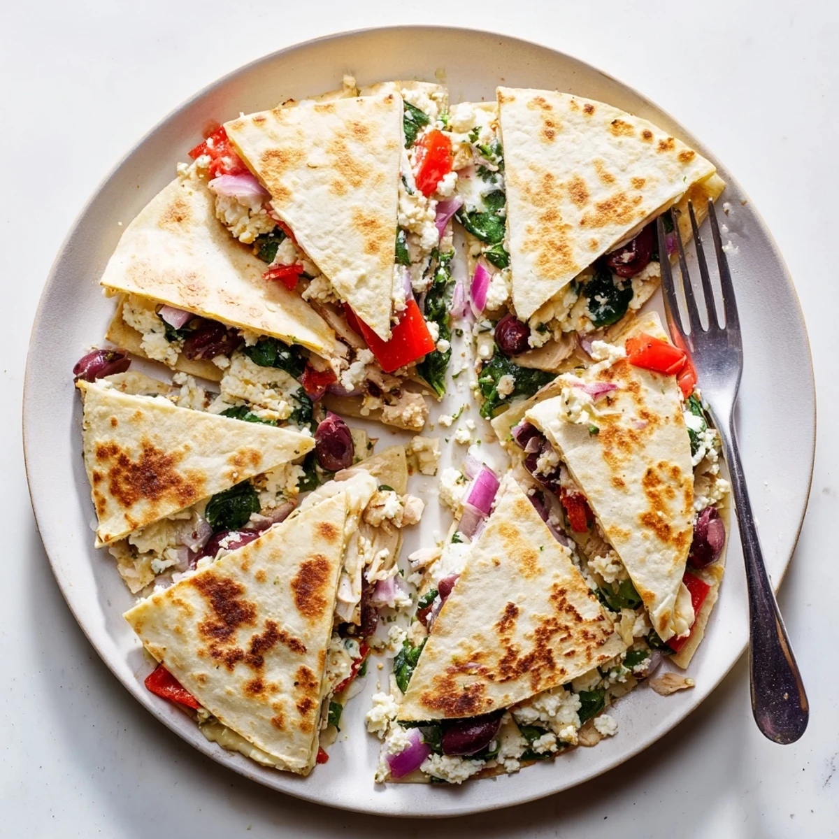 Sliced quesadilla wedges revealing juicy Greek marinated chicken and Mediterranean vegetables inside