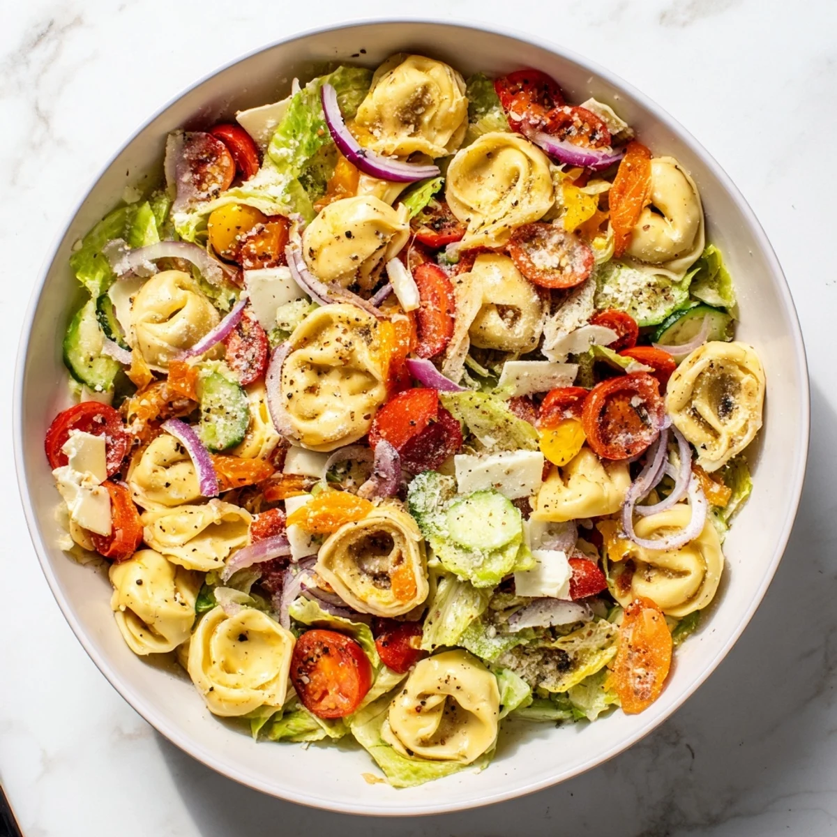Vibrant tortellini salad recipe topped with grated Parmesan, shredded lettuce, and roasted red peppers on a white platter