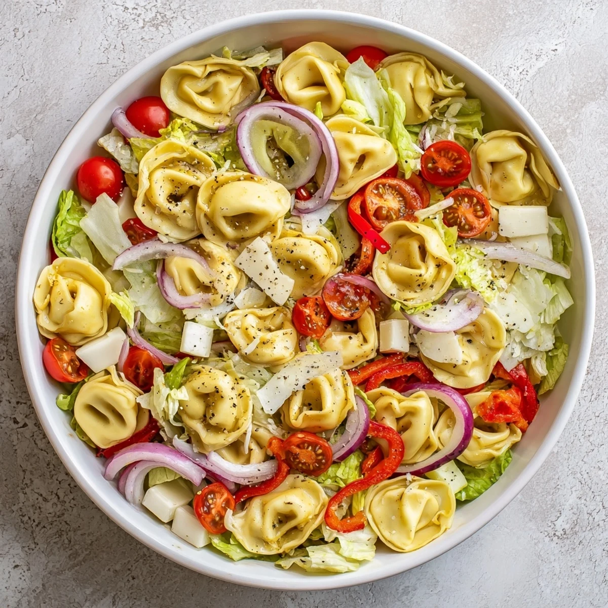 Hearty Italian-American grinder tortellini salad recipe featuring cherry tomatoes, provolone, and pepperoncini in a large serving bowl