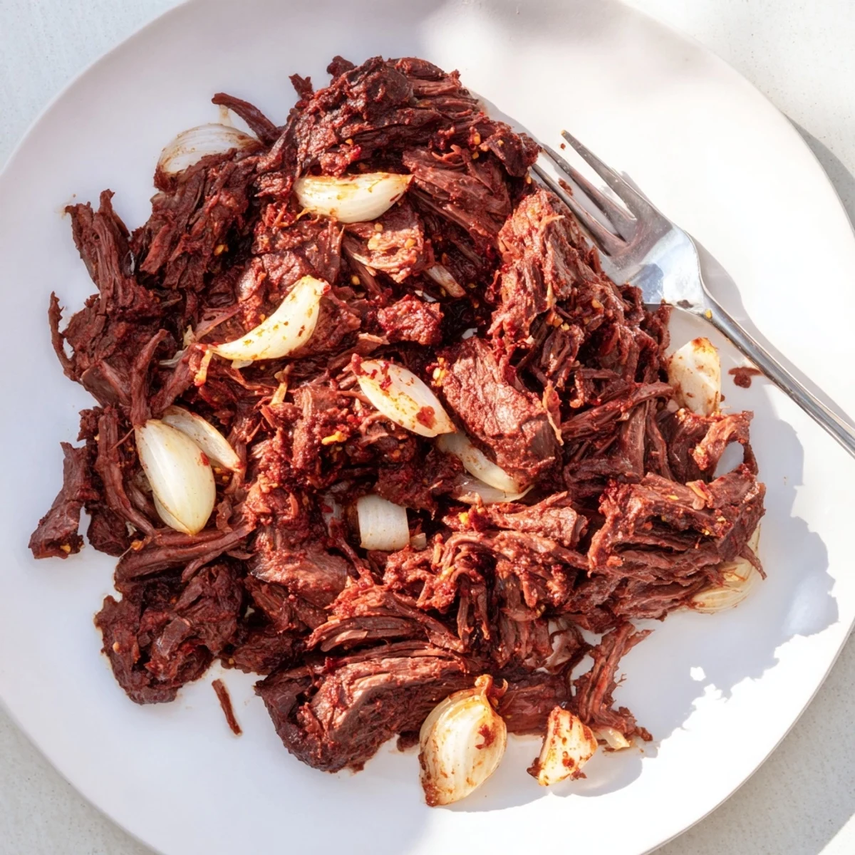 Tender slow cooker beef barbacoa shredded and piled high with fresh cilantro and lime wedges on a white platter
