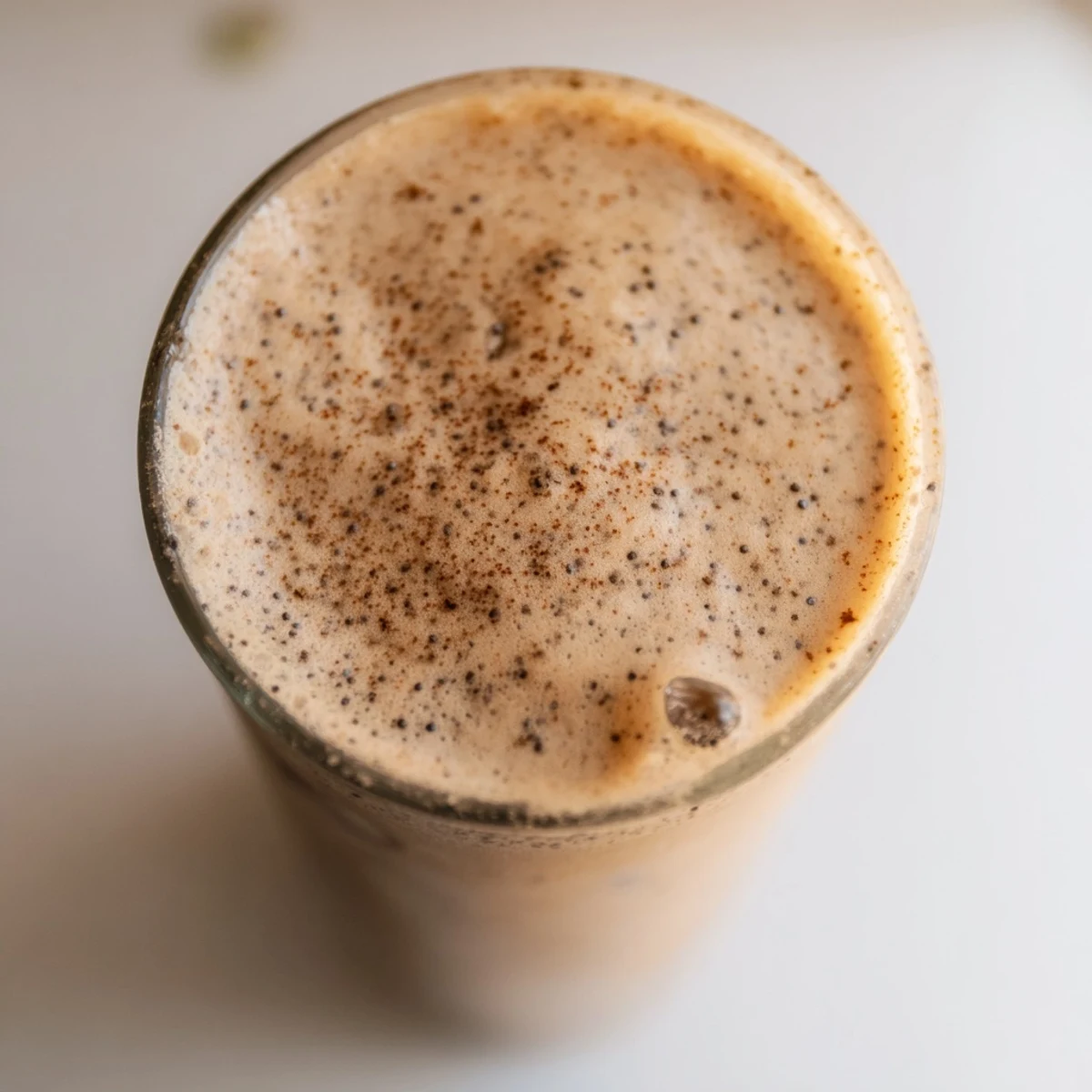 Creamy banana protein coffee smoothie topped with cinnamon in a tall glass