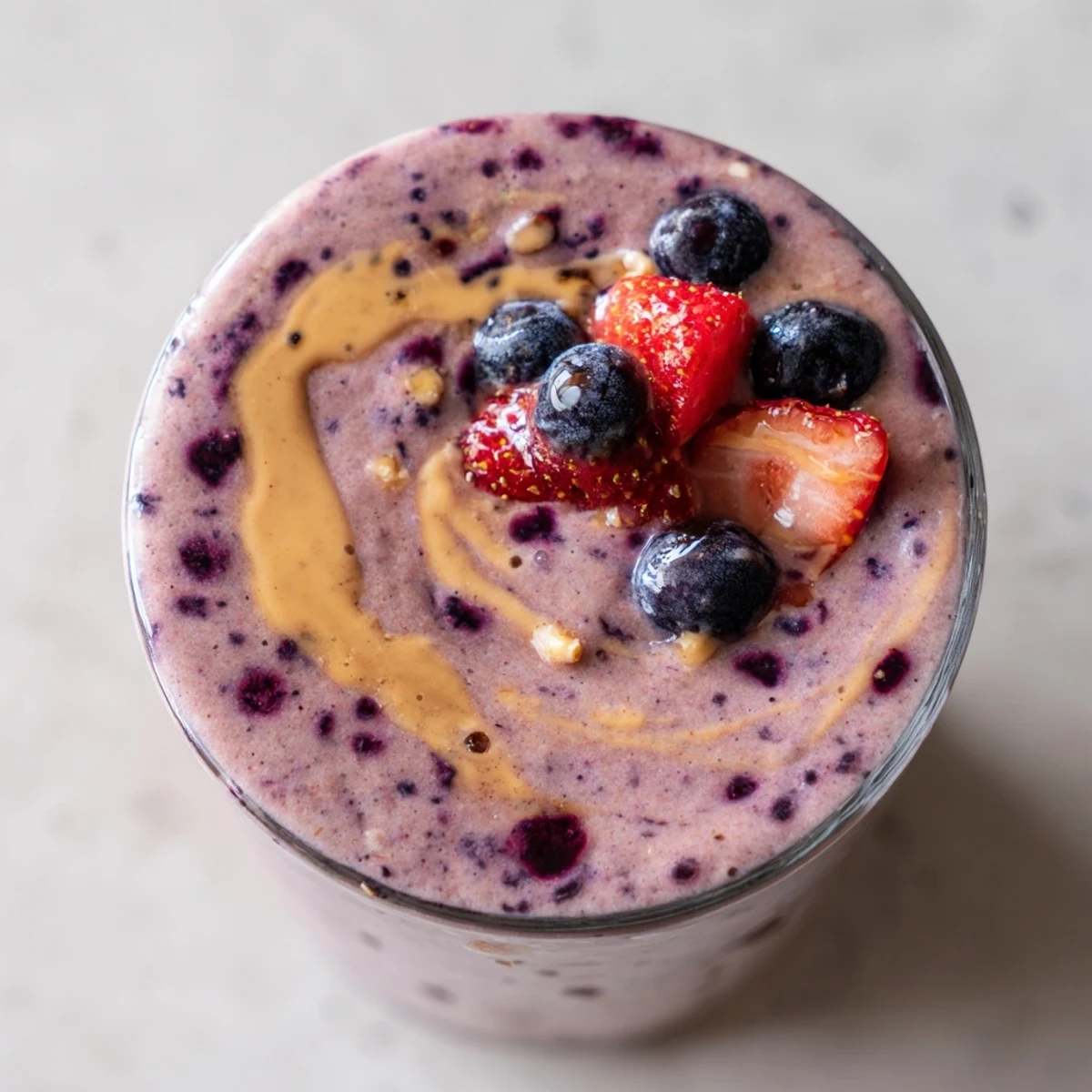 Thick purple peanut butter berry smoothie topped with fresh strawberries in a glass