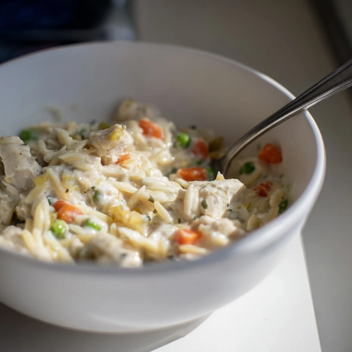Steam rises from a bowl of this comforting chicken pot pie orzo, garnished with fresh parsley and Parmesan.
