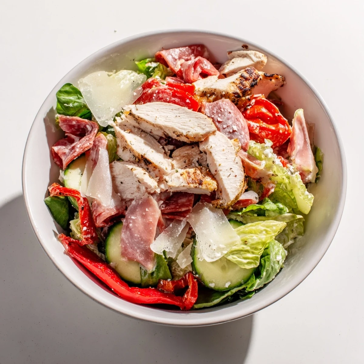 A bowl of Italian Grinder Chicken Salad piled high with salami, provolone, and tangy pepperoncini peppers.