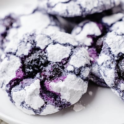 Golden crinkled blueberry cookies with powdered sugar tops cooling on a wire rack